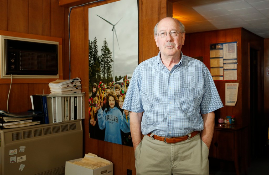 Chip Farrington, General Manager of the Fox Islands Electric Cooperative, poses for a photo in the cooperative's office next to a photo taken on the first day of the turbines started spinning. 