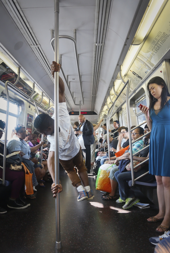 In this June 17, 2014 photo, Andrew Sanders, center, leader of the group W.A.F.F.L.E., which stands for We Are Family For Life Entertainment, performs acrobatic dance on a subway, in New York. His troupe, which has a shoe-brand sponsor and has been booked for music videos, parties, even a wedding, is reluctant to perform on subways because of police attention. (AP Photo/Bebeto Matthews)