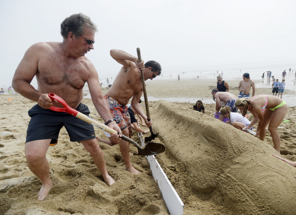 Phil Bonner of Hudson, Mass., left and Tom Curley of Stow, Mass., center, work with their team to build a sand sculpture of bottle rocket popsicle, during the competition in Ocean Park on Thursday. The team went on to win first place.