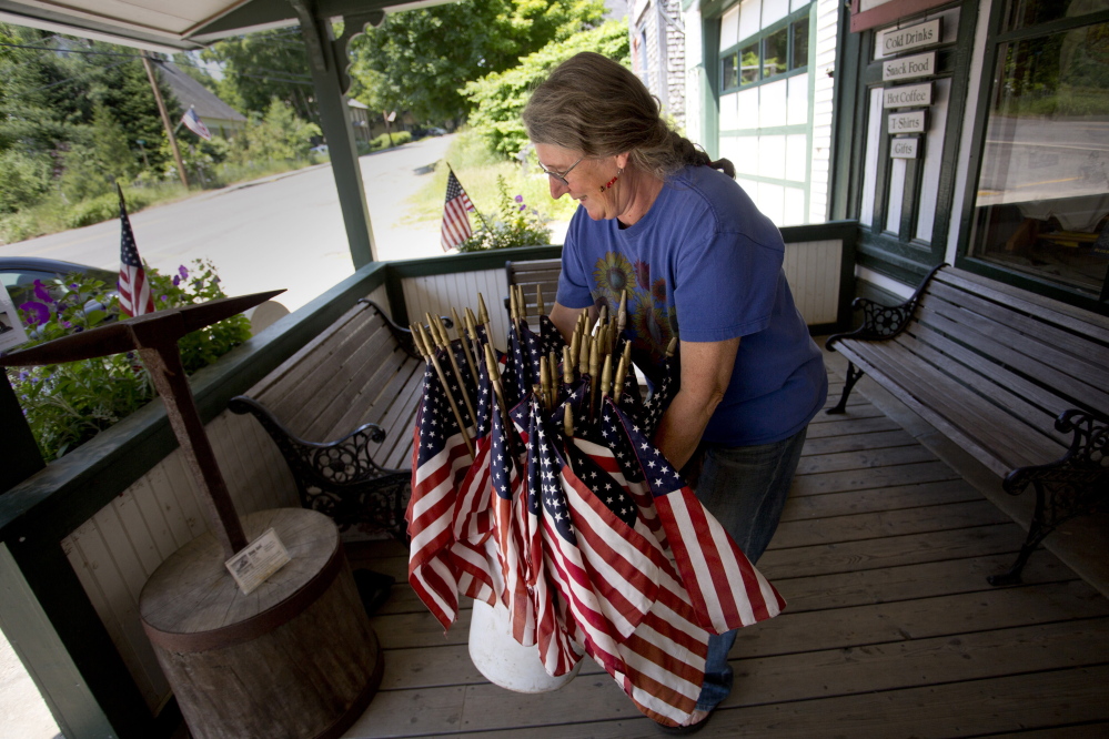 Sue Martin, an employee at Liberty Graphics in the Waldo County town of Liberty, sets out a collection of American flags, left over from the town’s Memorial Day celebration, on the store’s porch recently. She says she gives the flags away.