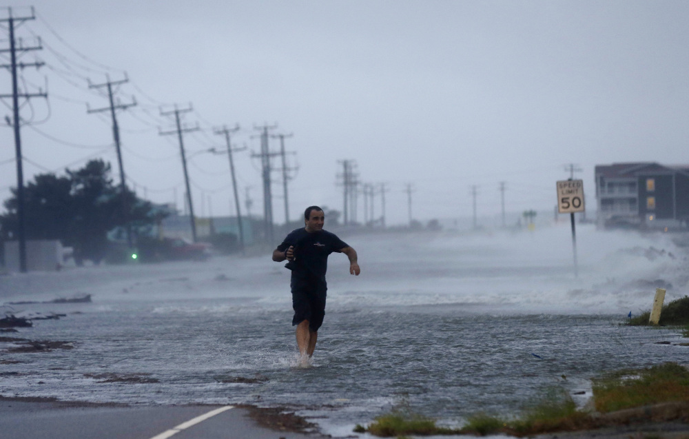 A man crosses a flooded Highway 64 as wind pushes water over the road as Hurricane Arthur passes through Nags Head, N.C., on Friday.