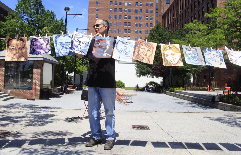 Dan Wood of South Portland helps to hang 26 portraits, painted by Lee Chisholm of Freeport, representing 26 of the 47 victims of the Lac-Megantic train disaster on Sunday, the first anniversary. Religious and environmental activists held a vigil in Congress Square Park to remember the victims of the Lac-Megantic train disaster.