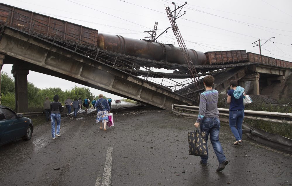 People walk under a destroyed railroad bridge over a main road leading into the east Ukraine city of Donetsk, near the village of Novobakhmutivka,  20 km North from the city of Donetsk, eastern Ukraine Monday.