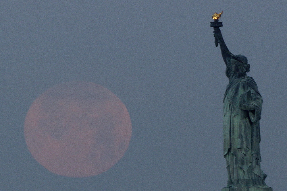 A “supermoon” sets near the Statue of Liberty on June 23, 2013. A larger-than-normal moon called a supermoon happens Saturday.