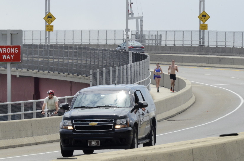 A bicyclist and runners use the barrier-protected sidewalk over the Casco Bay Bridge on Tuesday, with the bike lane marked by a white line alongside vehicle traffic. The Maine DOT says pedestrians who cross the bridge during repairs will have to use bike lanes.