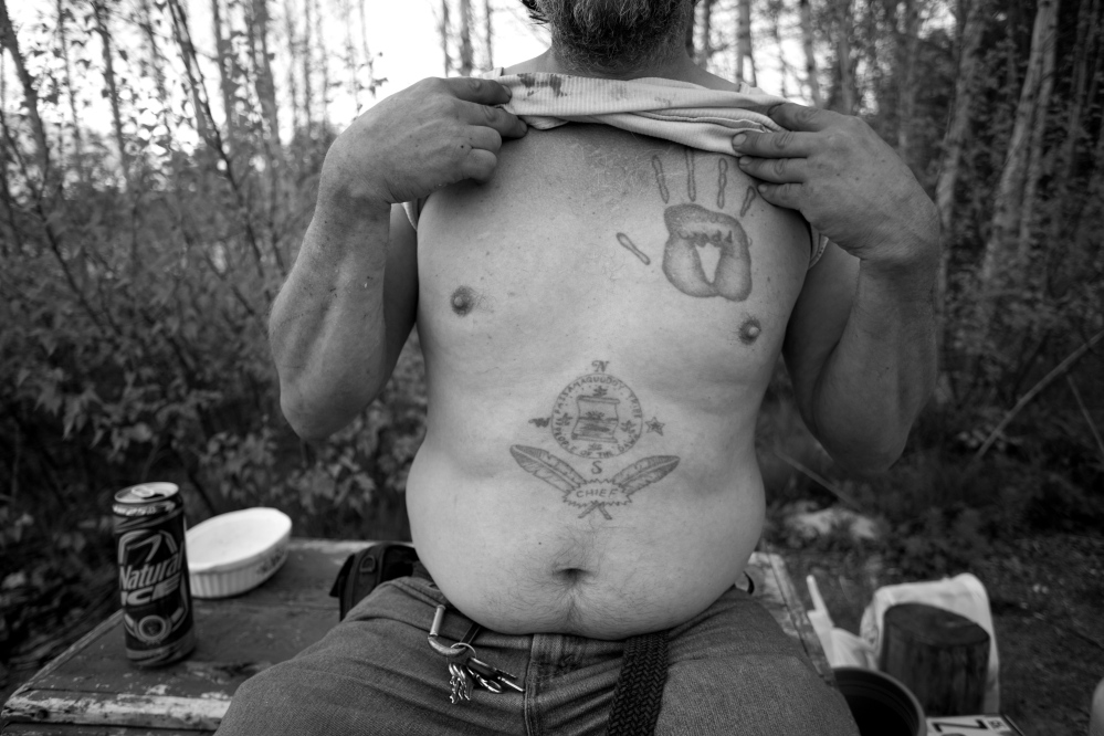 Ira Gilbert, a member of the Passamaquoddy tribe, shows the tattoos he got while in prison in Arizona. Today, Gilbert and his three dogs live in a mobile home on tribal land. Blame spread to many people in leadership roles in the 1980s and ’90s when votes for a tribal constitution ended in defeat.