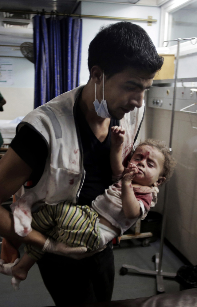 A medic carries a wounded girl in the emergency room of Shifa hospital in Gaza City. About 60 kids have died in a week and a half of fighting.