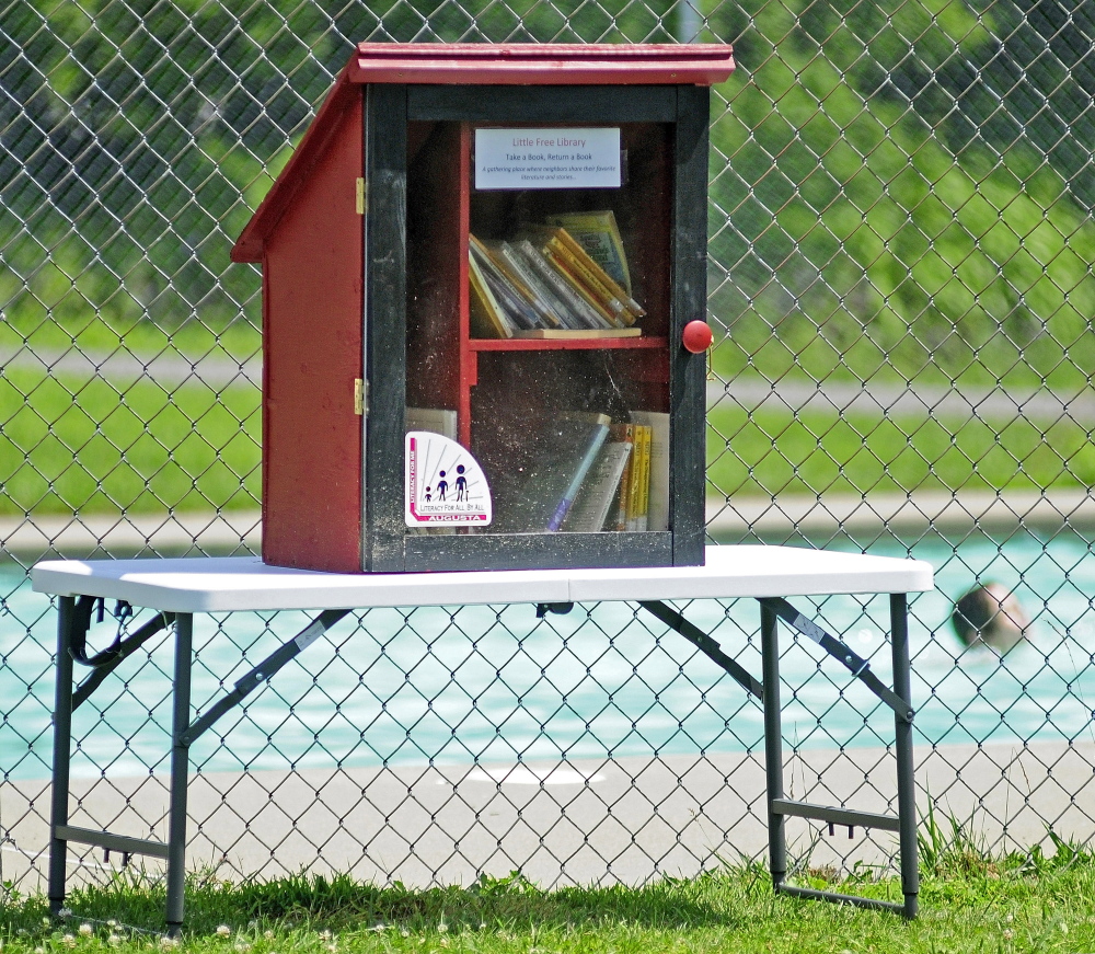 Children playing in the McCall’s Park pool are seen behind the Little Free Library on Friday in Augusta.