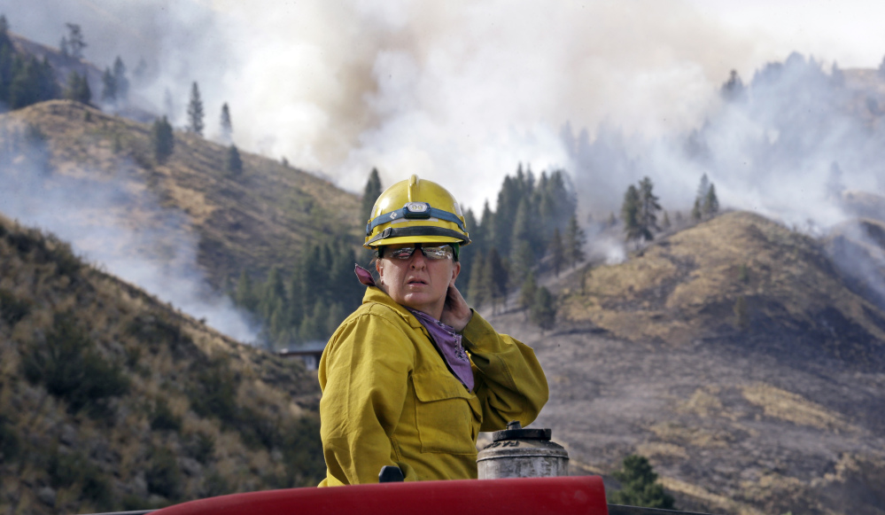 Firefighter Kathleen Calvin looks around as she sits atop her fire truck while waiting to begin work as smoke from a wildfire fills the sky behind on Saturday in Winthrop, Wash.