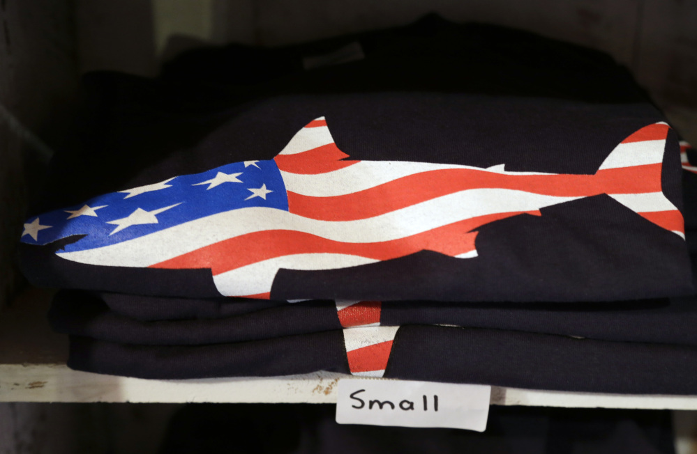 A T-shirt with a likeness of a shark incorporating an American flag rests on a shelf in a souvenir shop in Chatham, Mass.