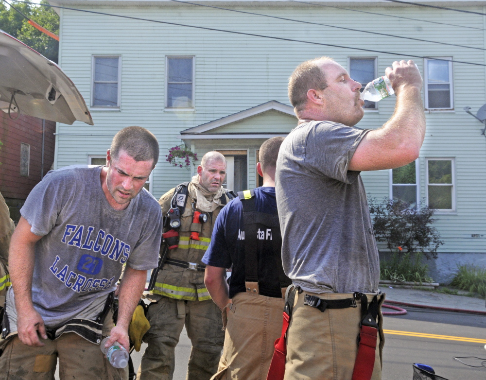 Firefighters pull off their gear and drink water Tuesday while battling a blaze in the attic of 32 State St. in Augusta.