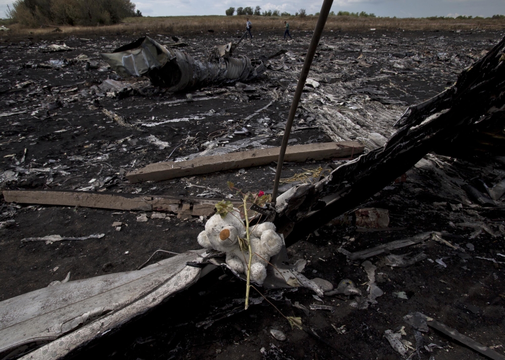 A toy bear is placed on charred plane fuselage parts, as people walk through the crash site of Malaysia Airlines Flight 17 near the village of Hrabove, eastern Ukraine, on Tuesday. A team of Malaysian investigators visited the site along with members of the OSCE mission in Ukraine for the first time since the air crash last week.