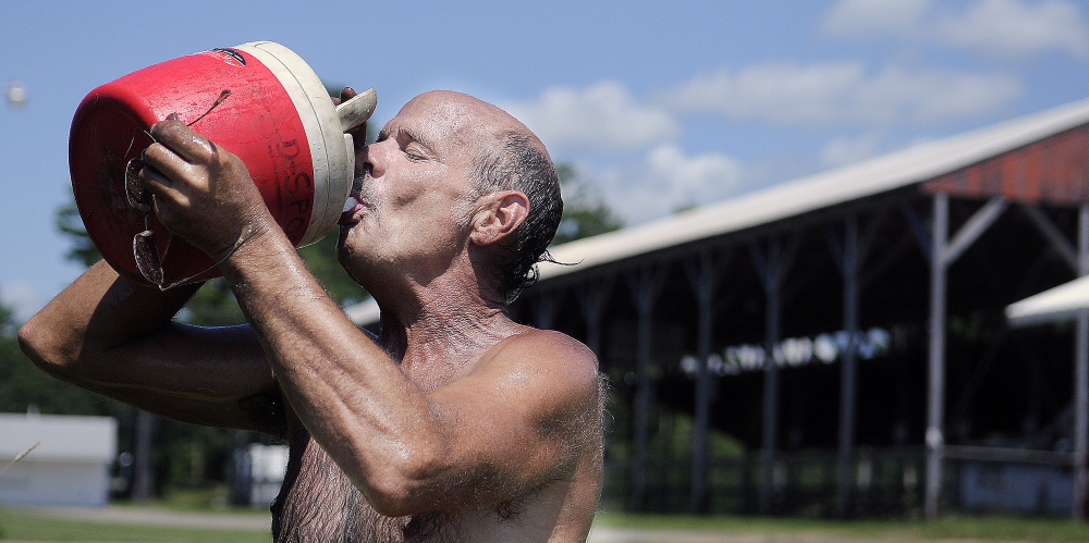 Carnival worker Bill Derick cools off with water Monday while setting up rides at the Pittston Fairgrounds. 