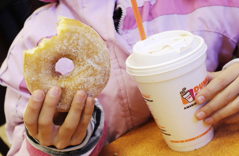 A girl holds a doughnut and a beverage at a Dunkin’ Donuts in New York. The company is pushing its cashiers to promote more items in the afternoon, when customers are more relaxed.