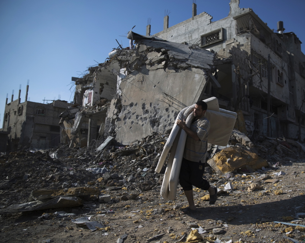 A Palestinian man carries salvaged belongings from damaged buildings in the Shejaia neighborhood of Gaza City on Sunday. Witnesses said the area was heavily hit by Israeli shelling.