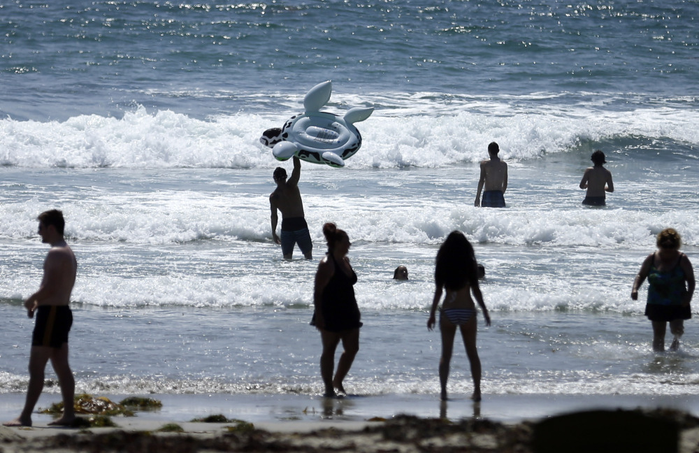 FILE - This, June 24, 2014, file photo shows people swimming on a sunny day at Mission Beach in San Diego. Stop sunbathing and using indoor tanning beds, the acting U.S. surgeon general warned in a report that cites an alarming 200 percent jump in deadly melanoma cases since 1973. (AP Photo/Gregory Bull, File)