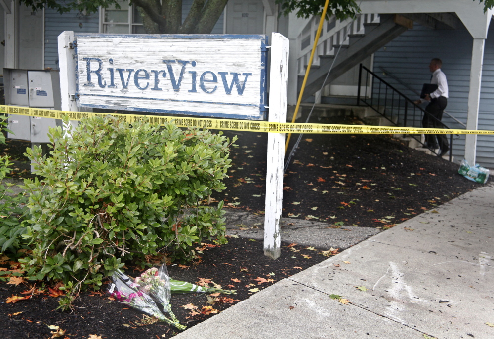 Bouquets of flowers rest at the RiverView apartment building sign Sunday as an investigator climbs the stairs to the apartment where Joel Smith killed his three children and his wife Saturday before fatally shooting himself.