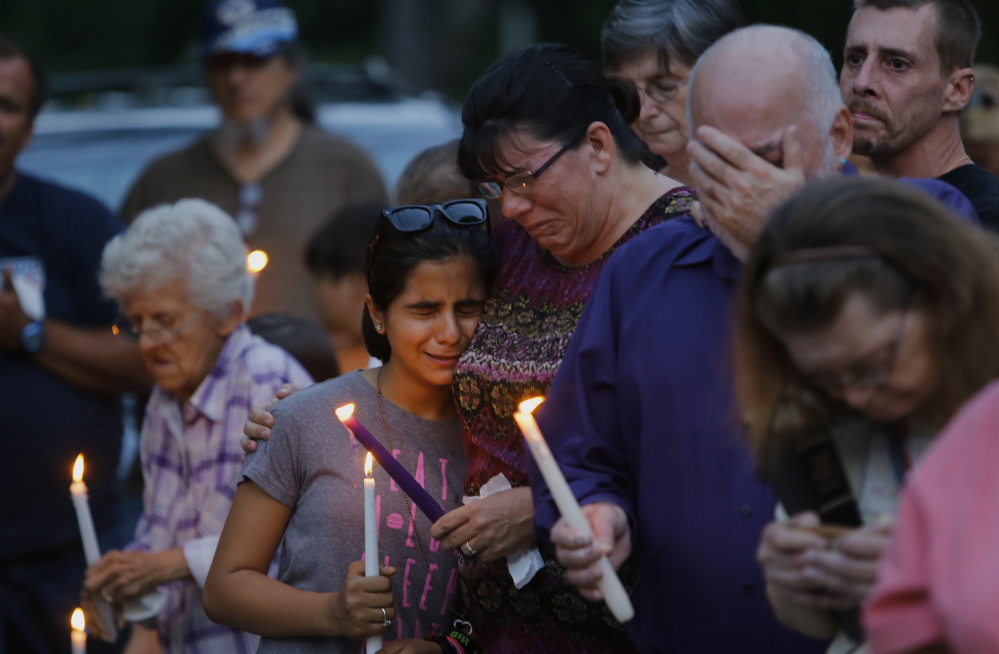 A family friend, Becca Garland, comforts 12-year-old Youna Karim during a vigil Tuesday evening for the Smith family outside RiverView Apartments in Saco. Authorities called Saturday’s murder-suicide – which claimed five lives, three of them children – one of the worst incidents of domestic violence in state history. At right, Steve Smith, the father of the man who killed his family, Joel Smith, covers his face.