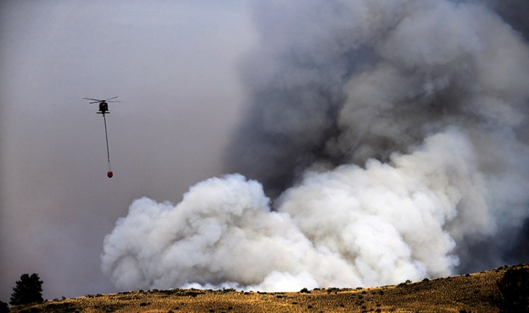 A helicopter preparing to drop water is dwarfed by a billowing cloud of smoke from a wildfire Friday, July 18. The Associated Press