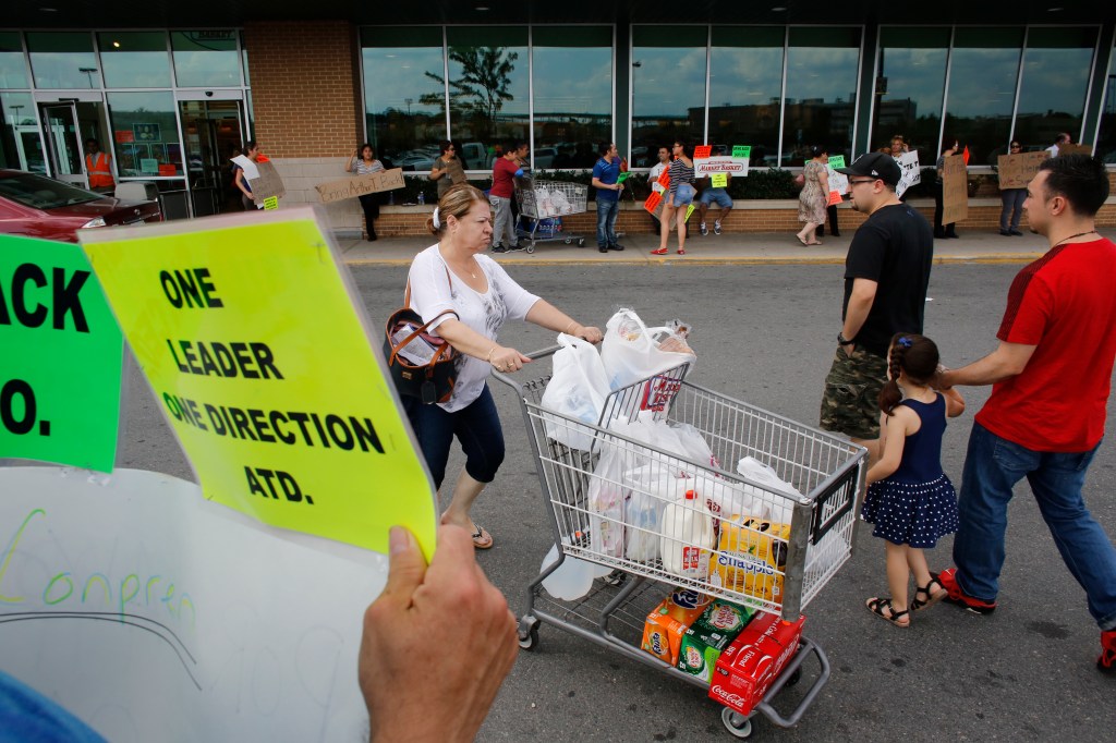 Demonstrators display placards outside a Market Basket grocery store as a shopper pushes a grocery cart on Tuesday in Chelsea, Mass. Supporters and employees rallied at Market Basket locations calling for Arthur T. Demoulas to be reinstated as CEO. 