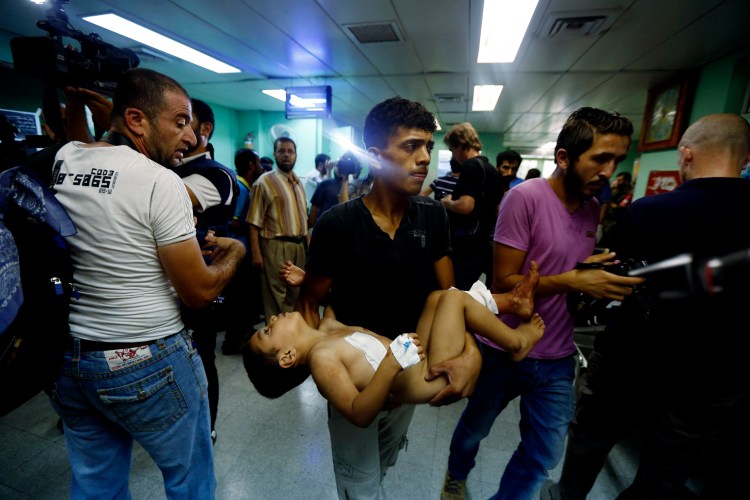 A Palestinian man carries a child, who was wounded in an Israeli strike on a U.N. school compound in the Gaza Strip, toward the emergency room of the Kamal Adwan hospital in Beit Lahiya, Thursday, The Associated Press