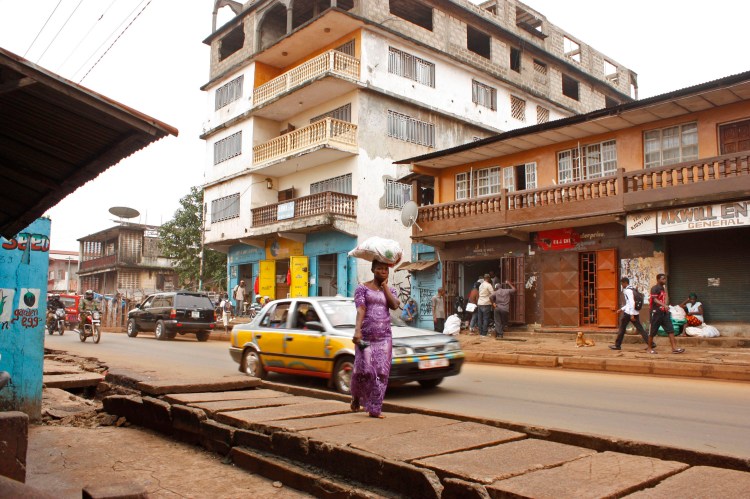 in this photo taken on  July 15, 2014,  a woman  walks near the Arwa clinic, center background,  that was closed after the clinic doctor got infected by the Ebola virus in the capital city of Freetown, Sierra Leone. The Associated Press