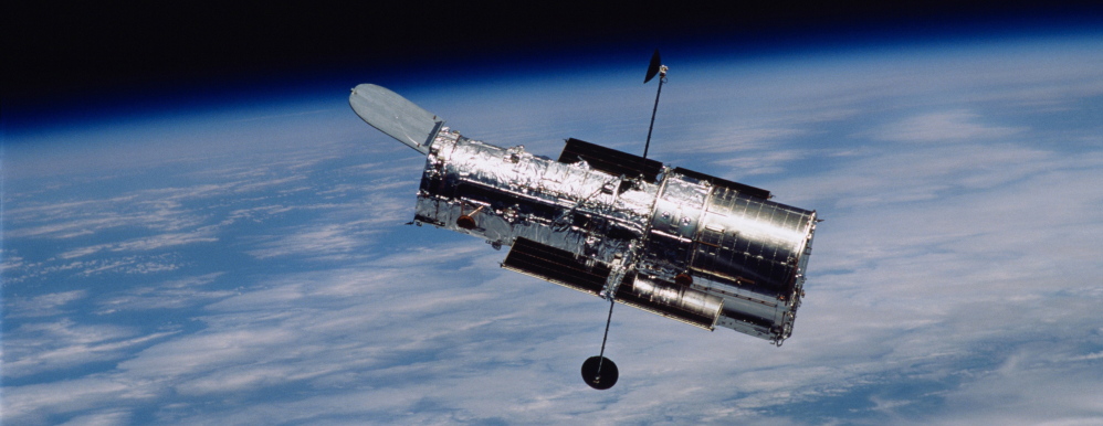 The Hubble Space Telescope flies above the Earth. Scientists using it can see star formation 10.7 billion light years away through a newly discovered “lensing” galaxy.