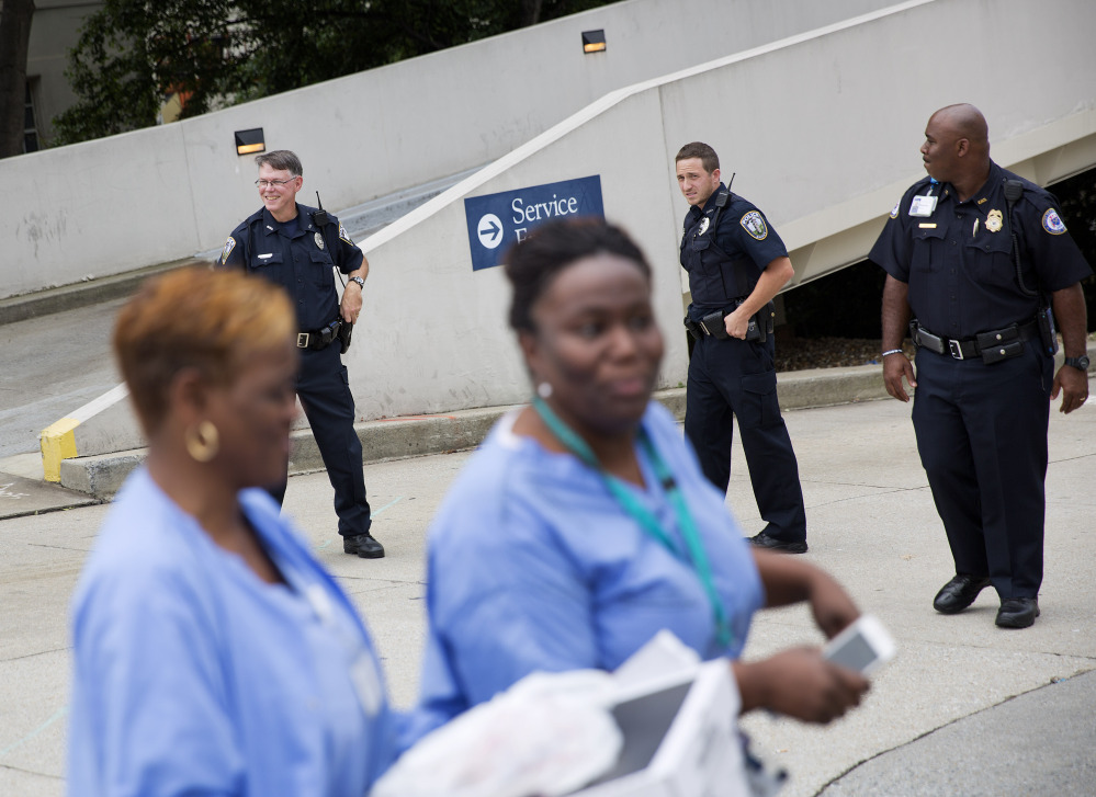 Hospital workers pass police officers guarding an entrance to Emory University Hospital.