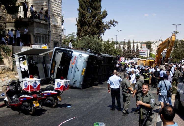 Israelis stand near a flipped bus at the scene of an attack in Jerusalem, Monday.