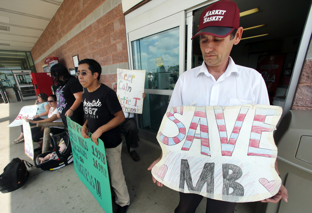 Ardian Zoto, right, an employee of Market Basket for six years, holds a sign outside the supermarket in Danvers, Mass., on Monday.