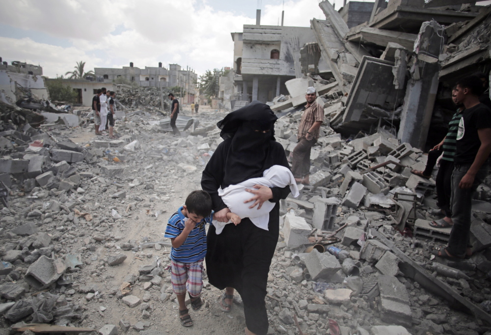 A Palestinian woman leads a boy past people inspecting the rubble of destroyed houses following Israeli strikes in Rafah refugee camp in the southern Gaza Strip on Monday. A pause in hostilities elsewhere did not apply to Rafah.