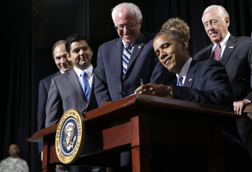 President Barack Obama, flanked by Senate Veterans Affairs Committee Chairman Sen. Bernie Sanders, I-Vt., left, and House Minority Whip Steny Hoyer of Md., right, signs the Veterans’ Access to Care through Choice, Accountability, and Transparency Act of 2014, in Fort Belvoir, Va., on Thursday.