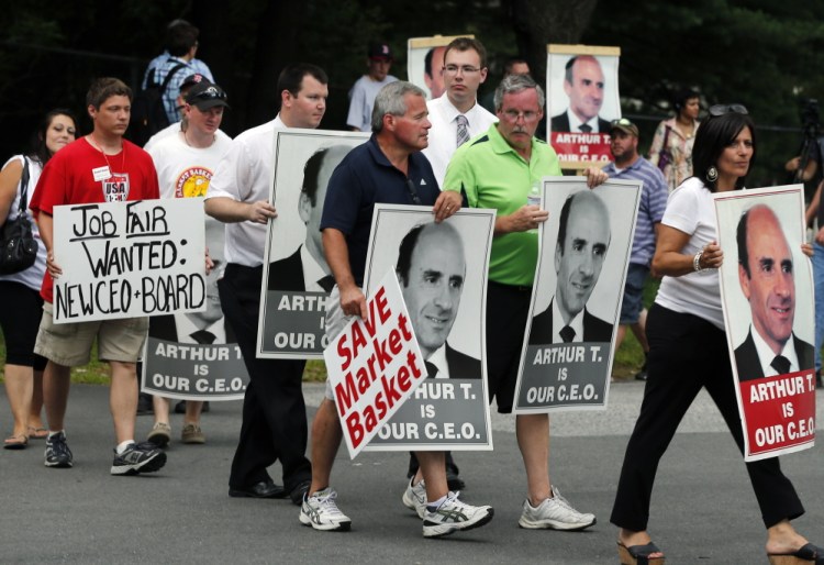 Protesters holding “Arthur T” signs picket outside a Market Basket supermarket job fair in Andover, Mass., on Monday. Market Basket stores in Maine, New Hampshire and Massachusetts have reportedly lost tens of millions of dollars in business since Arthur T. Demoulas was fired in June.
