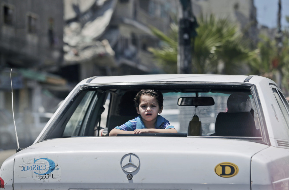 A Palestinian boy looks outside a car, back dropped, by the rubble of a house hit by an Israeli strike during the Gaza war, in Gaza City, Sunday.