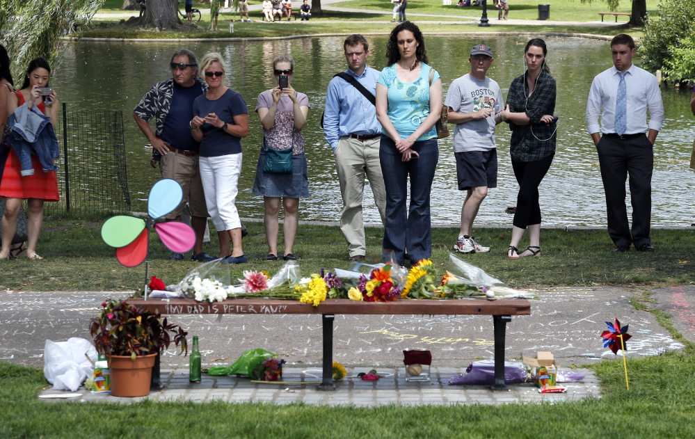 People pause by a bench Tuesday at Boston’s Public Garden, where a small memorial has sprung up at the place where Robin Williams filmed a scene during the movie “Good Will Hunting.” Williams, who won an Oscar for his role as a therapist in the film, died Monday in an apparent suicide.
