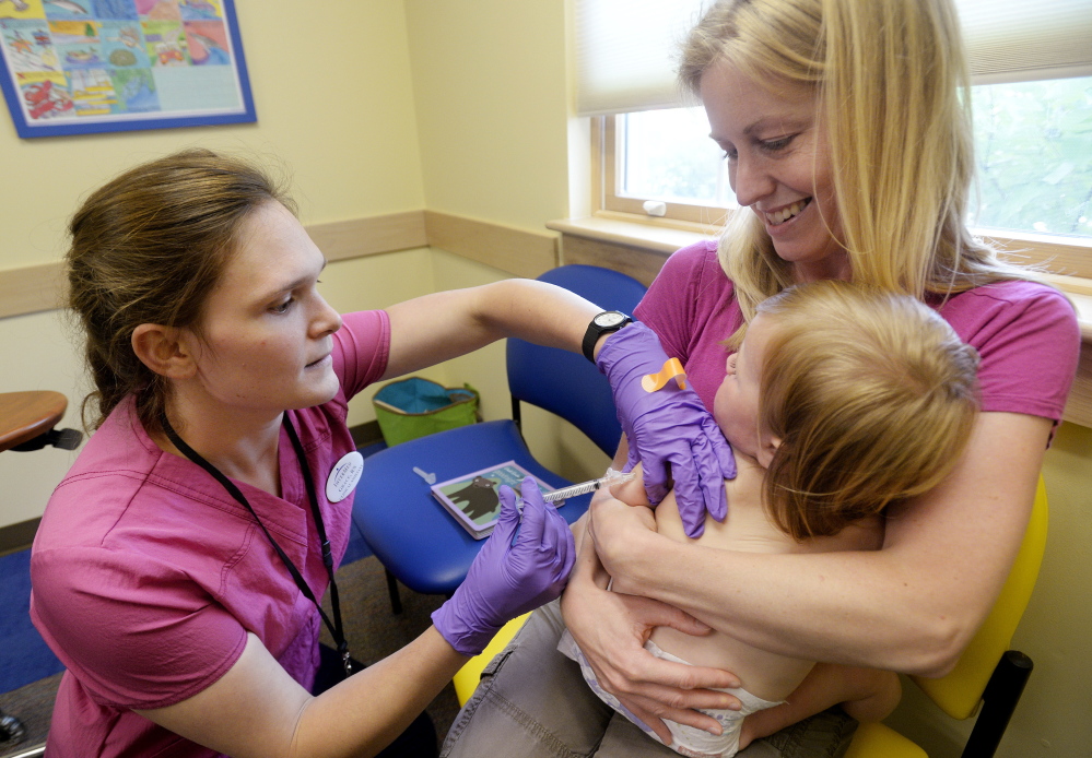 Amber Dugan of Durham holds her 16-month-old daughter, Tessa, as she is vaccinated by Grace Montgomery, a registered nurse, at InterMed in Yarmouth last month. Parents who choose not to have their children vaccinated are making a decision that’s leading to a resurgence in childhood diseases.