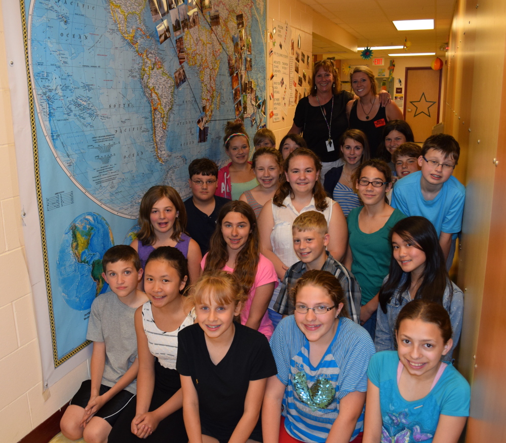 Wells Junior High School sixth-graders meet world traveler and alumna Katie McDonough (rear, right) and Katie’s mother, Kim McDonough (rear left), following Katie’s eight-month adventure. The group is posing by  a large map in the school hallway, where students marked Katie’s travels around the world.