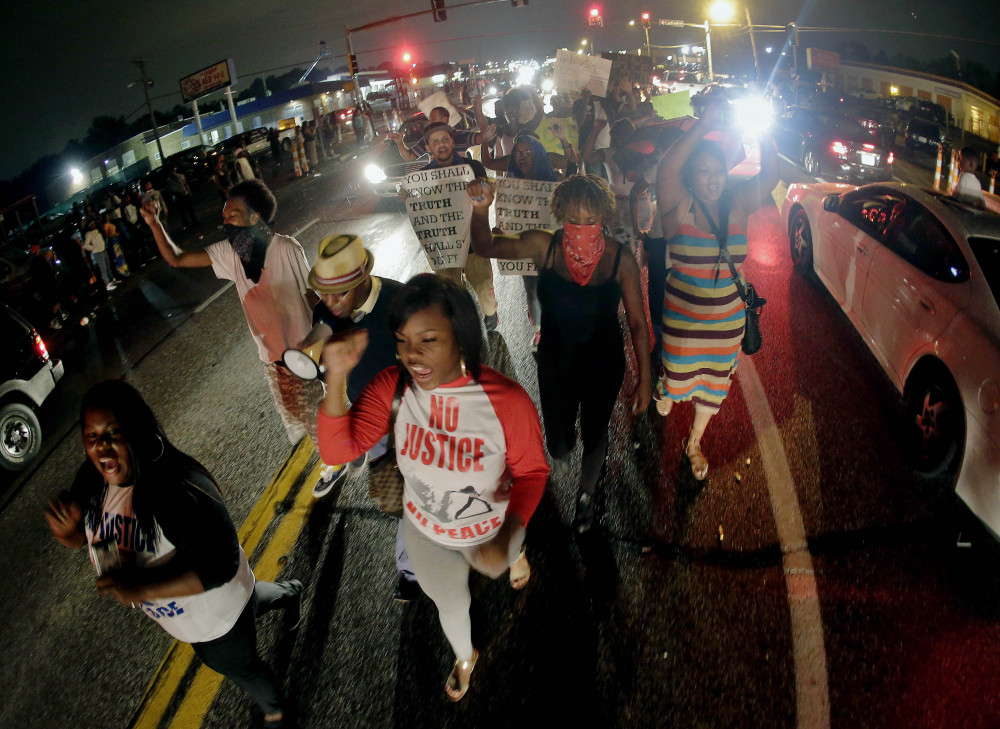 In this Friday, Aug. 15, 2014 file photo, protesters march down the middle of a street in front of a convenience store in Ferguson, Mo. that was looted and burned following the shooting death of Michael Brown, an unarmed black teenager, by a white police officer on Saturday, Aug. 9.