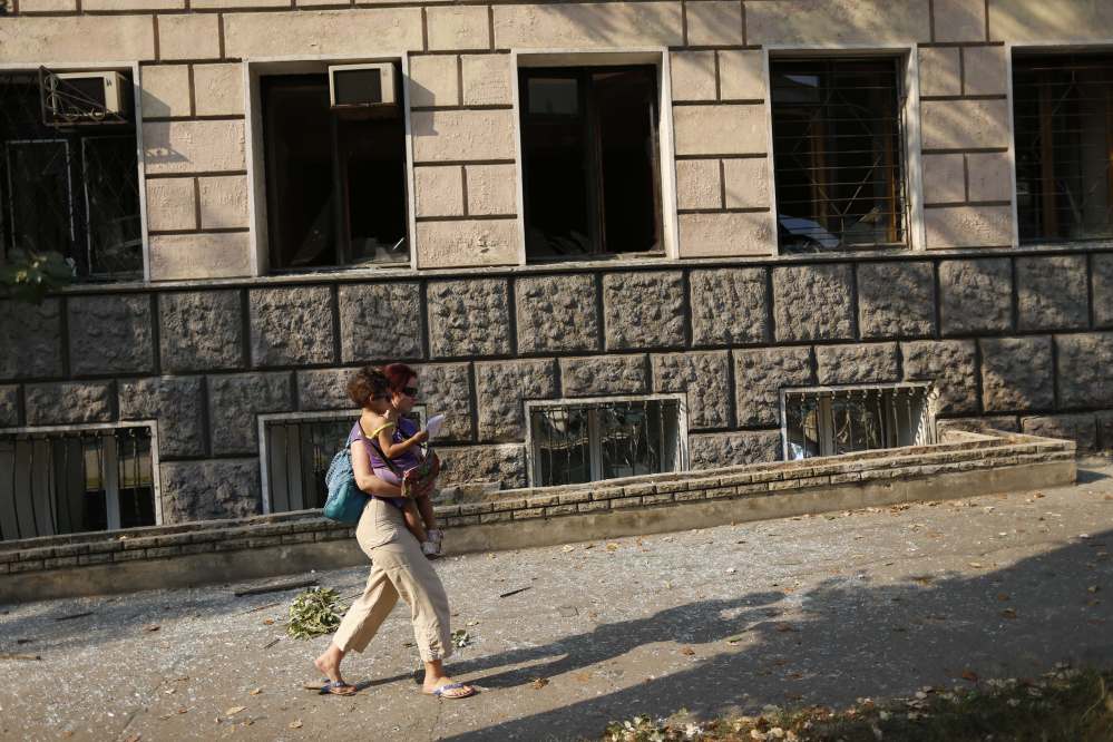 A woman with a child walks past an apartment building damaged by shelling in the center of Donetsk, eastern Ukraine, Thursday, Aug. 14, 2014. Ukrainian forces stepped up efforts to dislodge the separatists from their last strongholds in Donetsk and Luhansk, with more heavy shelling overnight.
