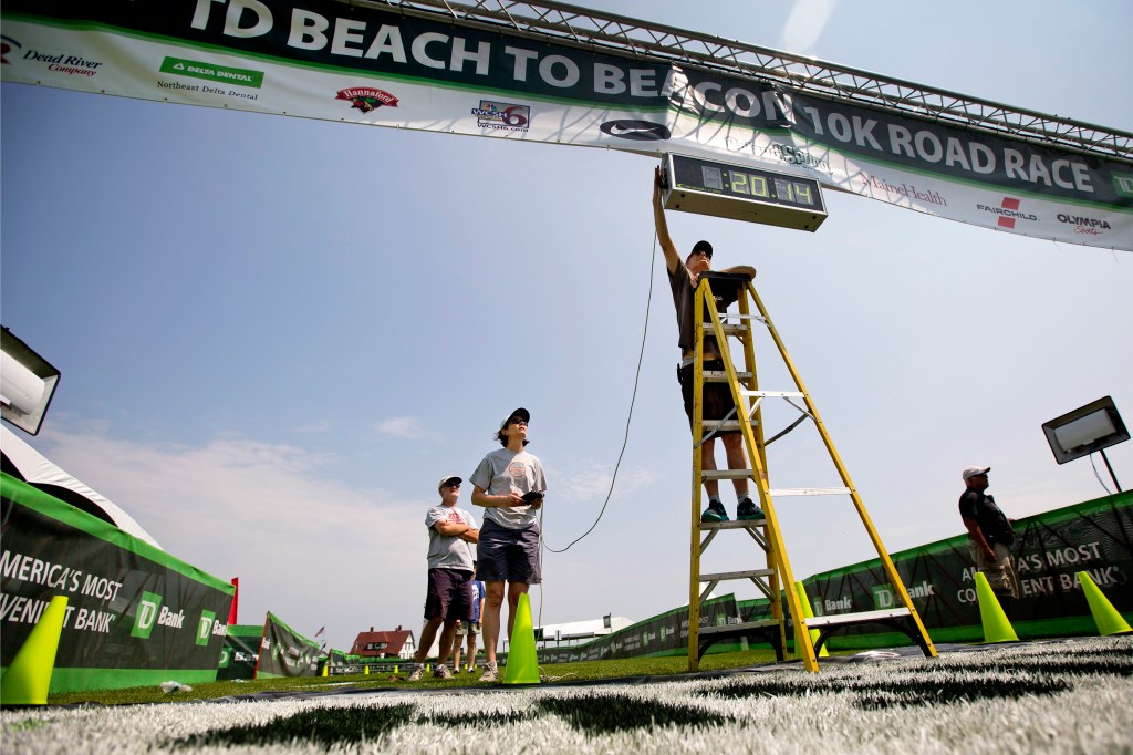 Bob Teschek, owner of Granite State Race Services, attaches a wire to the race clock after hanging it above the finish line of the TD Beach to Beacon 10k at Fort Williams Park on Friday.