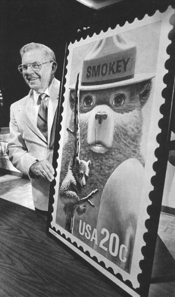 Ray Bell, the man who cared for Smokey Bear after the young cub was rescued from a forest fire 50 years ago, is shown with an oversized copy of the Smokey Bear stamp.
