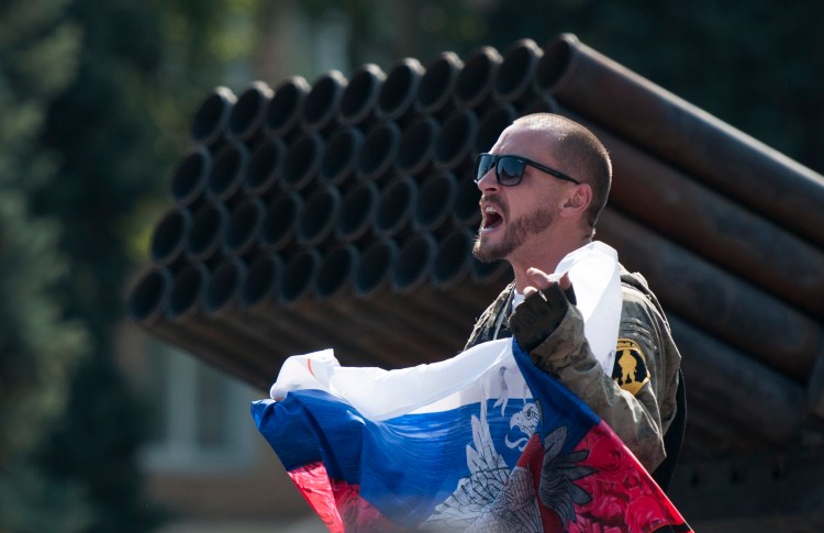 A pro-Russian rebel holds a Russian national flag near damaged heavy hardware from the Ukrainian army during a demonstration in the central square in Donetsk, eastern Ukraine, on Sunday. Ukraine has retaken control of much of its eastern territory bordering Russia in the last few weeks, but fierce fighting for the rebel-held cities of Donetsk and Luhansk persists.