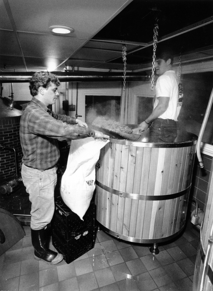 Ed Stebbins holds open a sack as Richard Pfeffer shovels spent grain from a mash tank at Gritty McDuff’s brewery in Portland. Congressional intervention will allow brewers to continue providing the byproduct to farmers for animal feed.