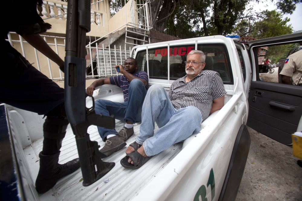 Michael Geilenfeld waits in handcuffs as the manager of his orphanage sits with him in the back of a police truck outside the St. Joseph’s Home For Boys after police closed it down in Port-au-Prince, Haiti, on Friday.