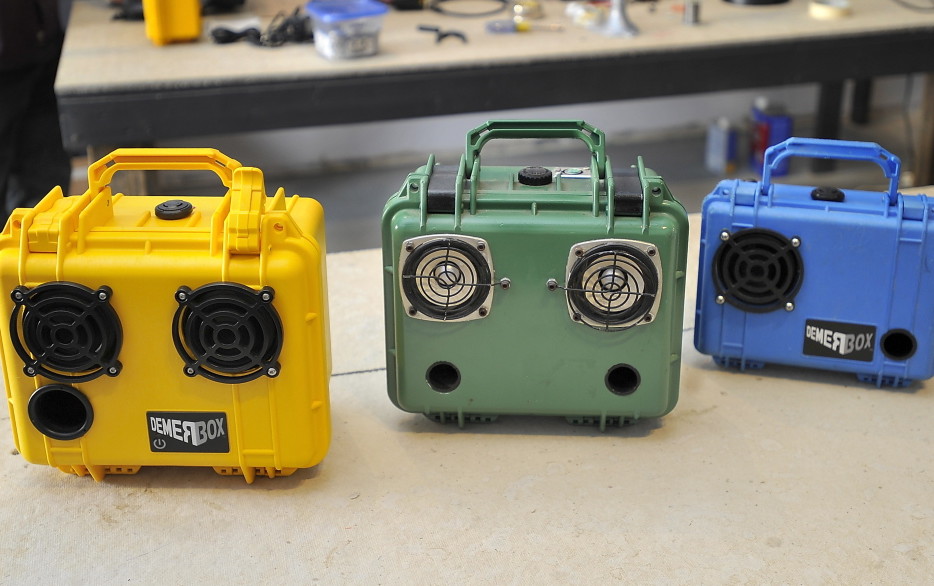 The DemerBox comes in two styles – The Bang, right, is the size of a lunchbox and has one speaker. The Big Bang, left, is larger and has two speakers. Center: the original prototype.