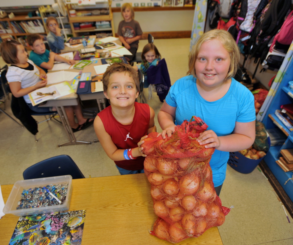Jacob Luff, left, and Eleanor King, fifth-graders at Albert S. Hall School in Waterville, hold some of the donated onions the class received after the loss of their garden project.