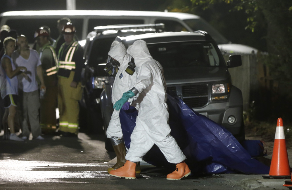 Investigators in protective clothing drag a tarp across the street in front of the house where a Massachusetts prosecutor said the bodies of three infants were found Thursday in Blackstone, Mass. Worcester County District Attorney Joseph Early Jr. said authorities don’t know when or how the babies died.