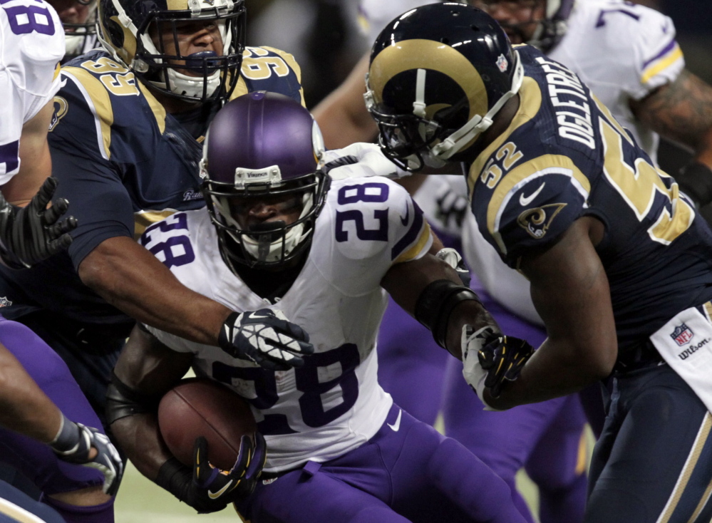 Minnesota Vikings running back Adrian Peterson runs with the ball as St. Louis Rams defensive tackle Aaron Donald, left, and linebacker Alec Ogletree, right, defend during the first quarter of their NFL football game Sunday in St. Louis.
