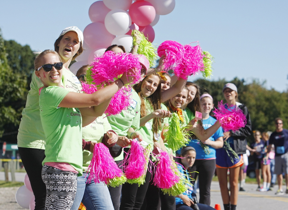 Volunteers cheer for runners as they near the finish line at the Race for the Cure on Back Cove in Portland on Sunday.