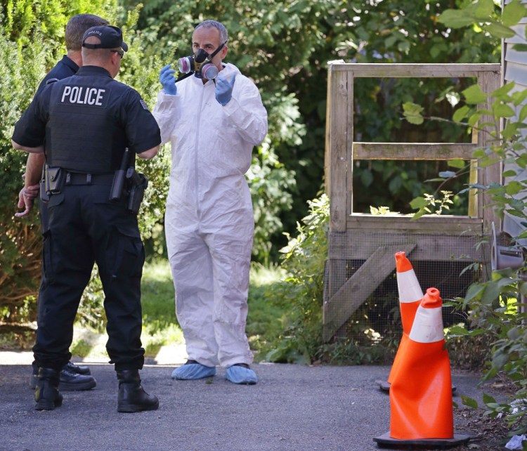 An exterminator, right, talks with a Blackstone police officer standing post and a member of the inspections services division of the Blackstone health department before entering through the back door of a house in Blackstone, Mass. on Friday where a prosecutor said the bodies of three infants were found earlier in the week.